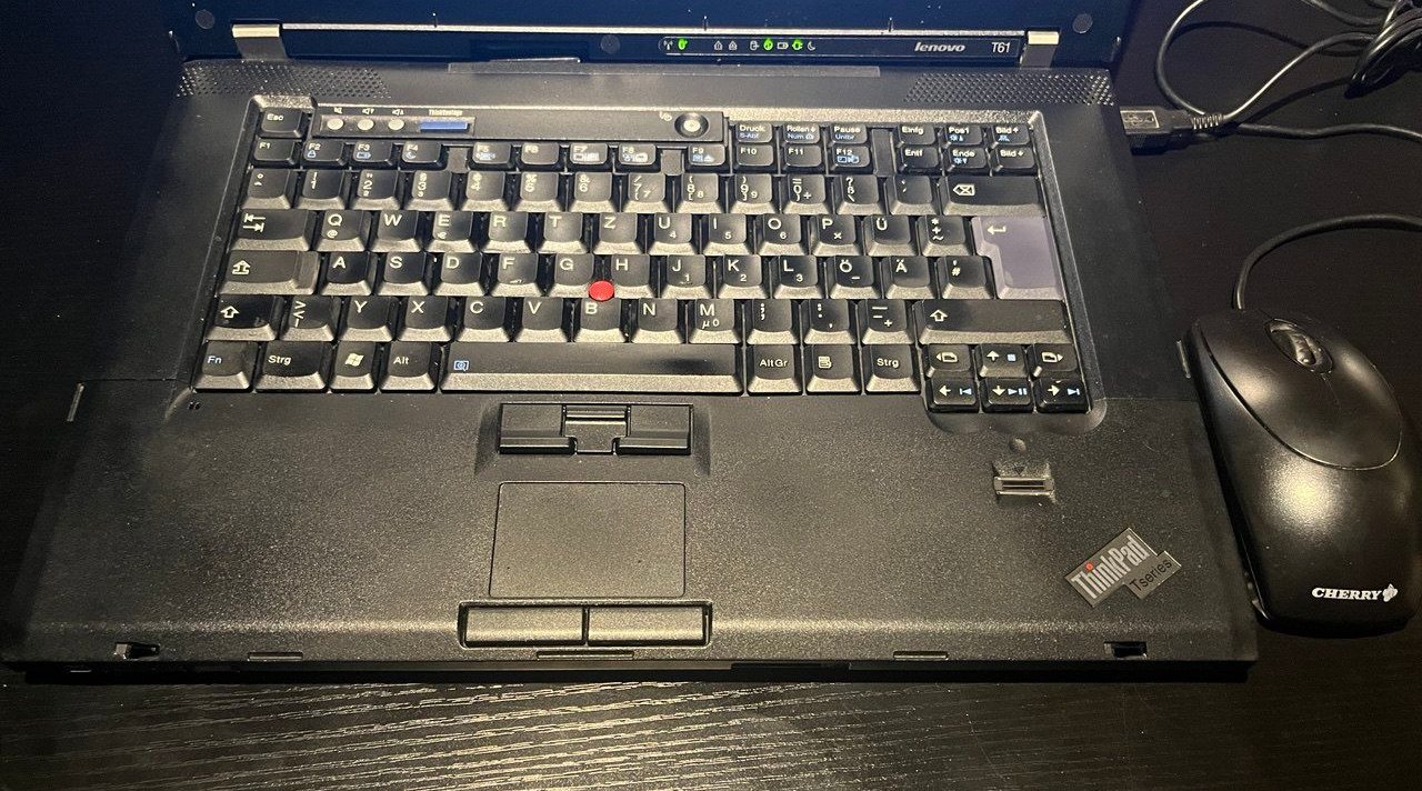 Black Thinkpad laptop with keyboard, mouse, and trackpad, on a desk.