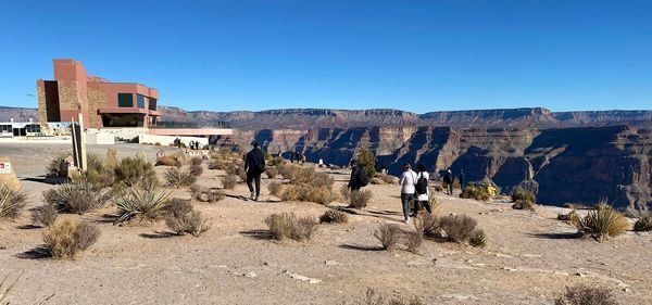 A group of people are walking in the desert near a building.