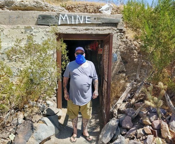 A man wearing a mask is standing in front of a mine entrance.