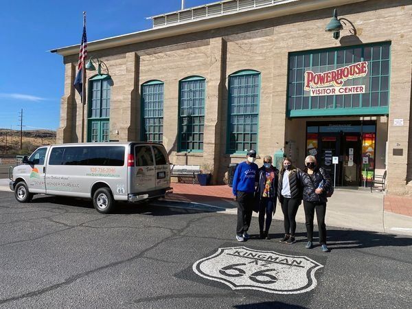 A group of people standing in front of a building with a van parked in front of it.