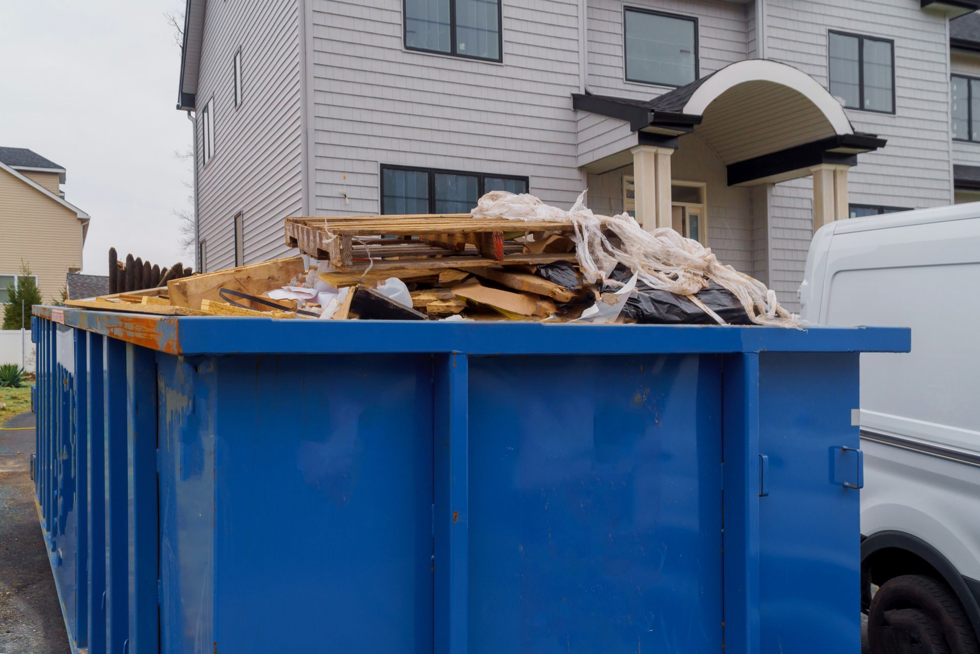 A large blue dumpster is sitting in front of a house.