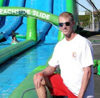 A man wearing sunglasses is sitting in front of an inflatable slide.