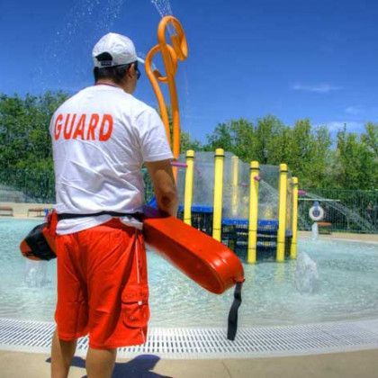 A lifeguard is standing next to a pool holding a life preserver