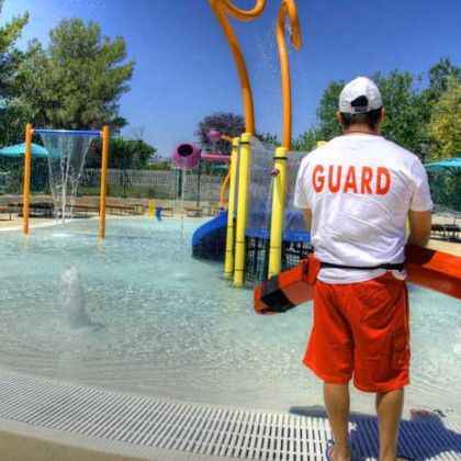 A lifeguard is standing in front of a water park holding a life preserver.