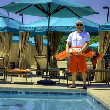 A lifeguard stands next to a swimming pool holding a life preserver