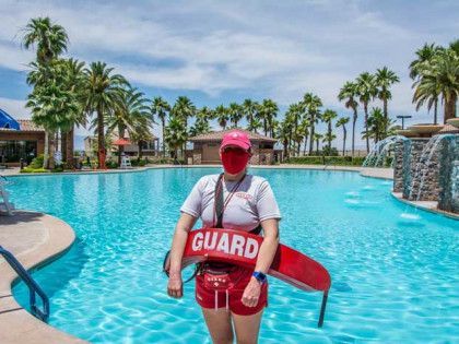 A lifeguard is standing next to a swimming pool holding a life preserver.