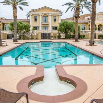 A large swimming pool surrounded by palm trees in front of a large building.