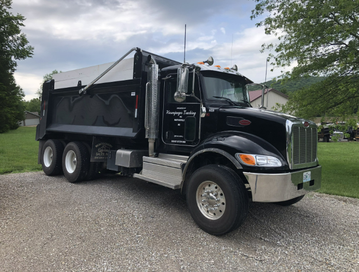 A black dump truck is parked on a gravel road.