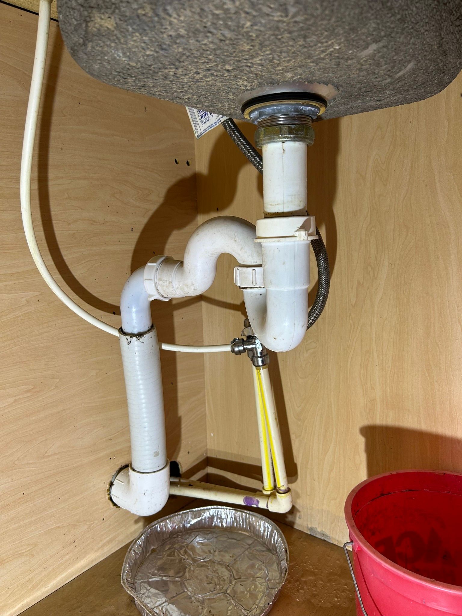 A sink with a drain pipe underneath it and a red bucket.