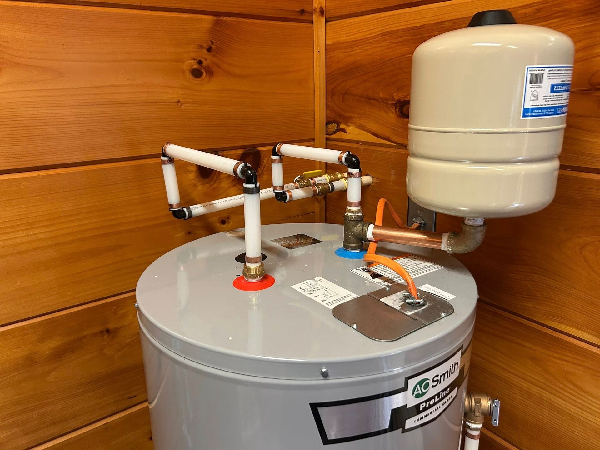 A water heater is sitting in a wooden room next to a wooden wall.