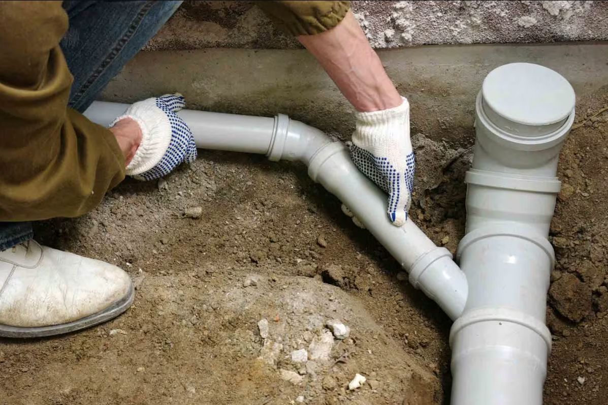 A black pipe is being installed in a trench of dirt.