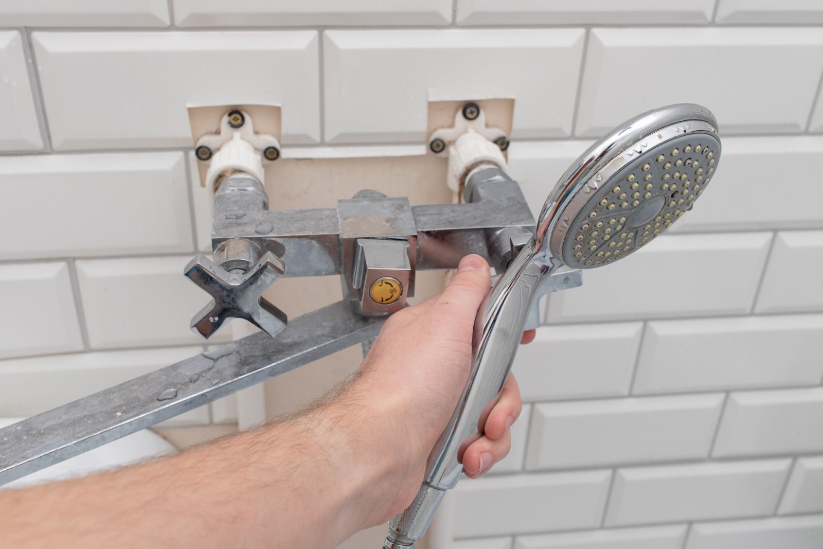 A person is fixing a shower head in a bathroom.