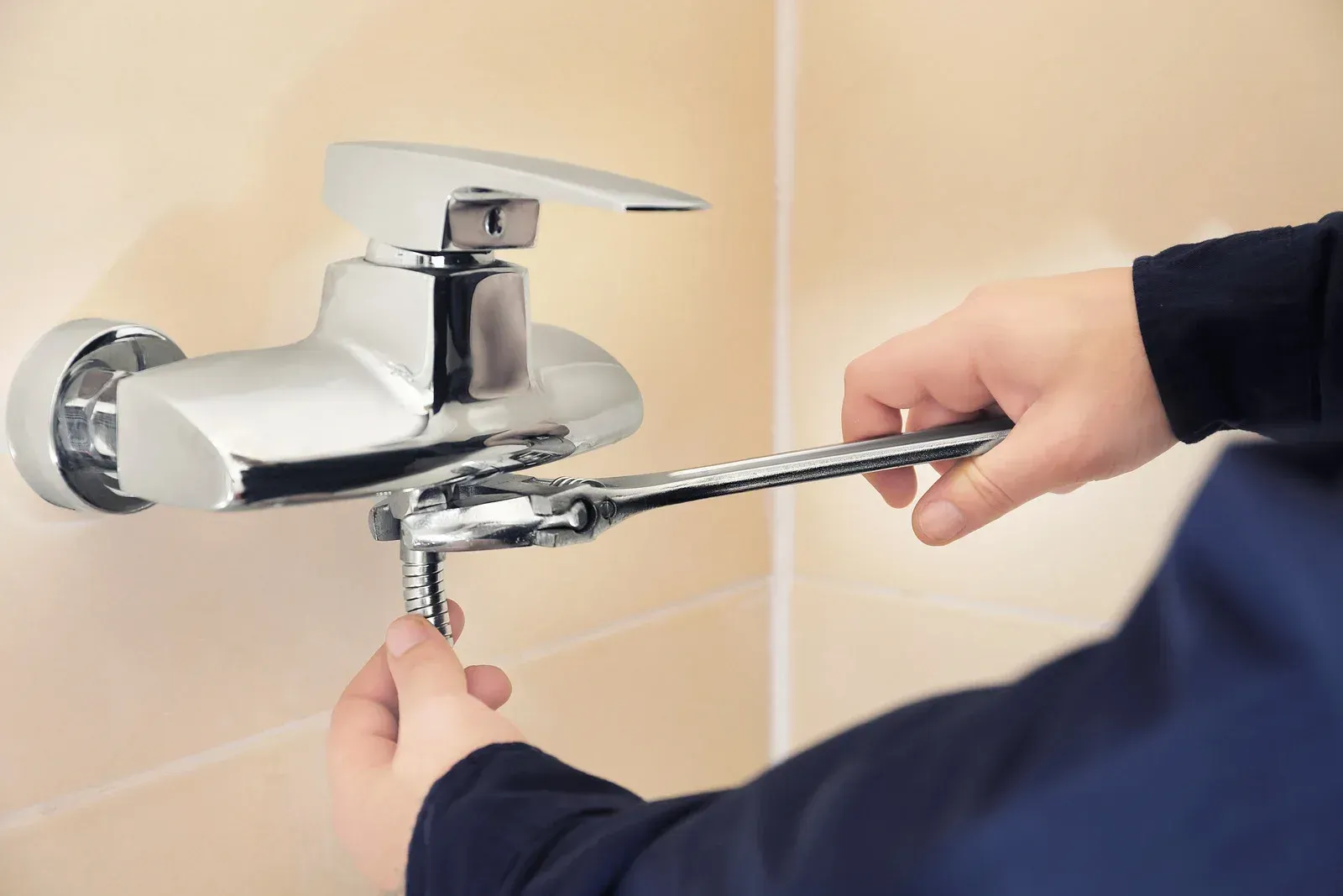 A person is fixing a faucet with a wrench.