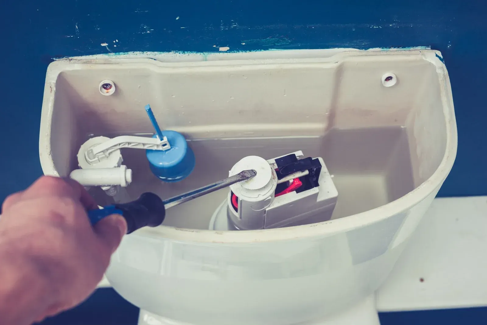 A person is fixing a toilet with a screwdriver.