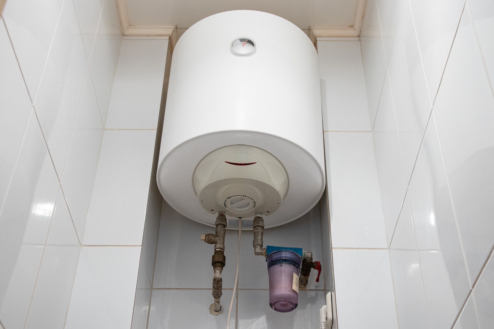 A white water heater is hanging from the ceiling in a bathroom.