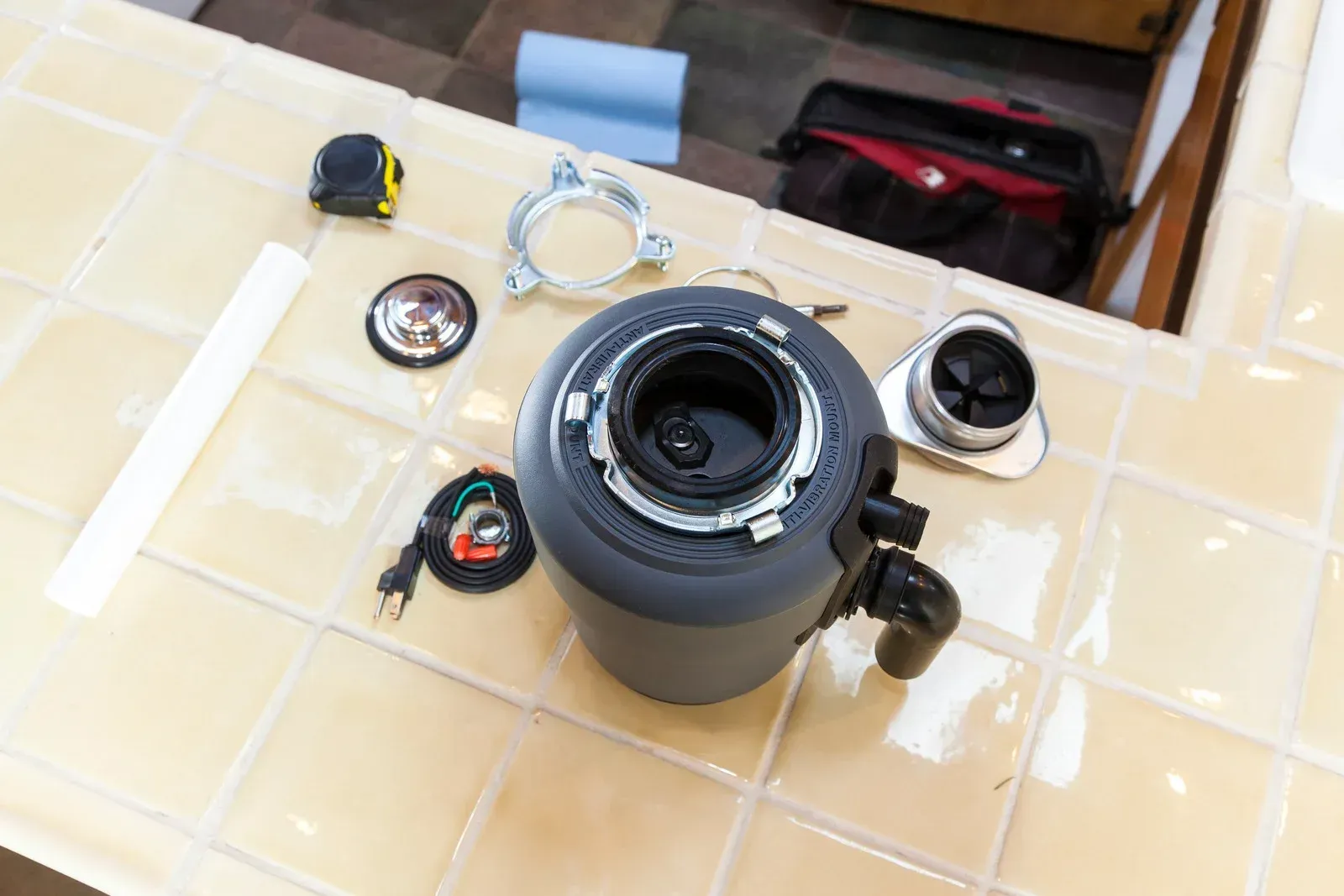 A garbage disposal is sitting on top of a tiled counter.