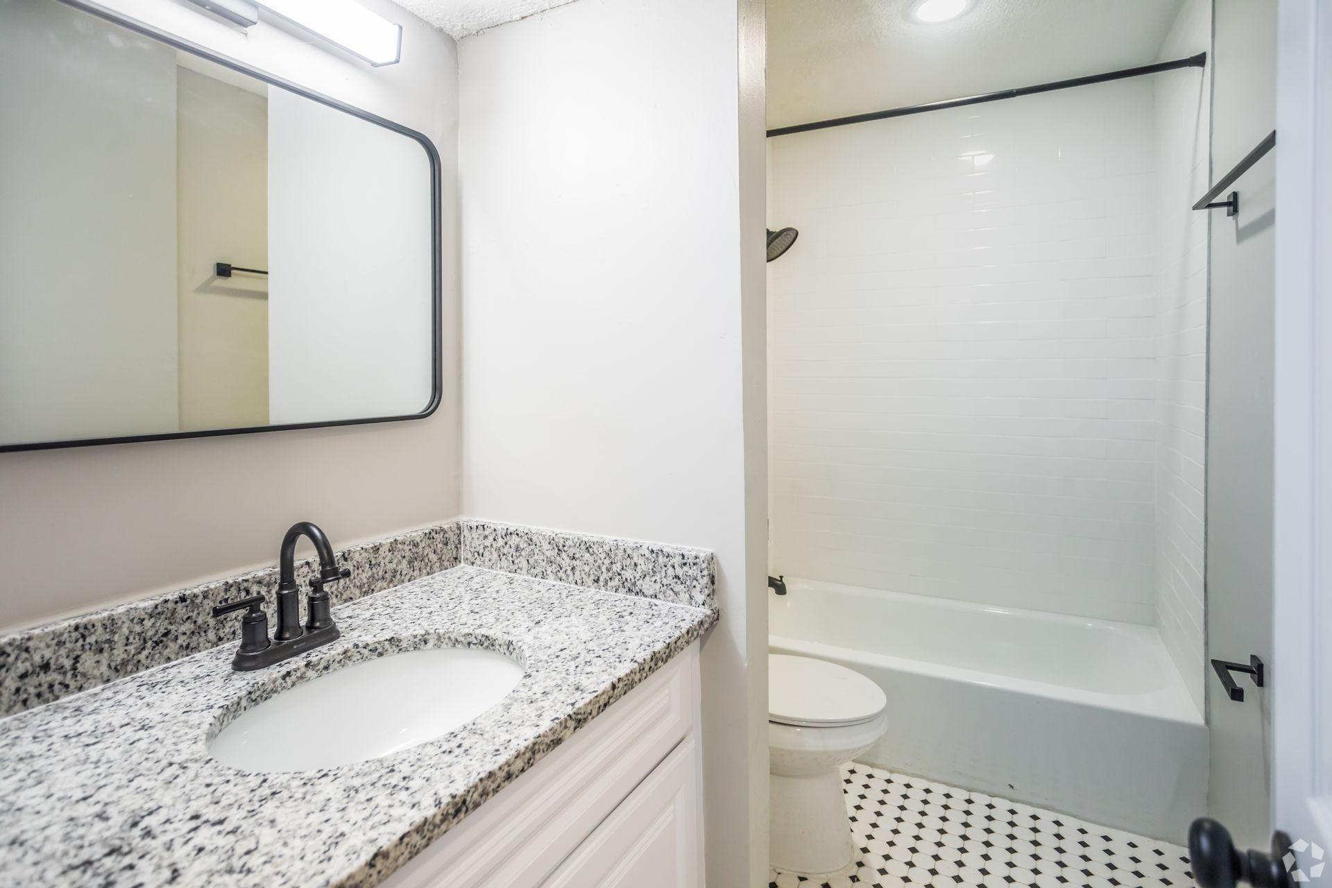 Bathroom with white walls, black fixtures, granite countertop, and white tile shower.