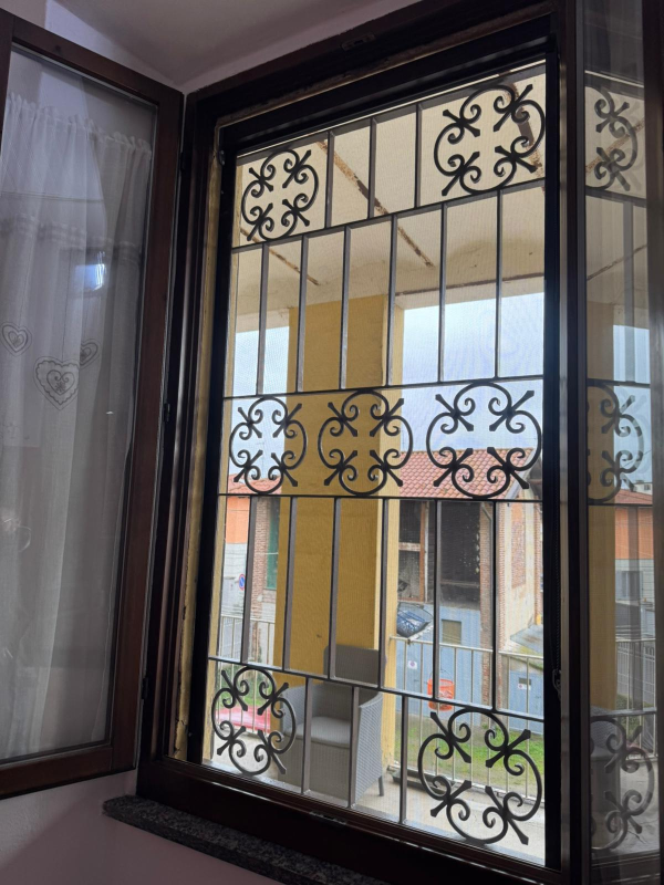 Una finestra con telaio in legno e grata di sicurezza decorativa in metallo con motivi circolari e a volute.