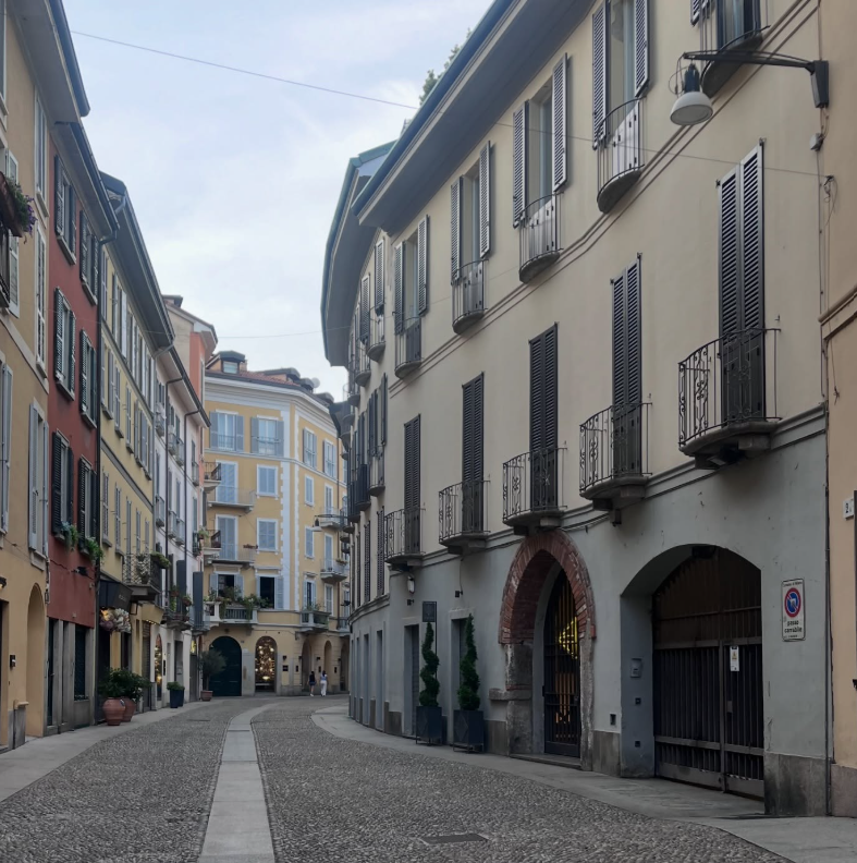 Una stretta via acciottolata in una città italiana, fiancheggiata da colorati edifici storici e portali ad arco.