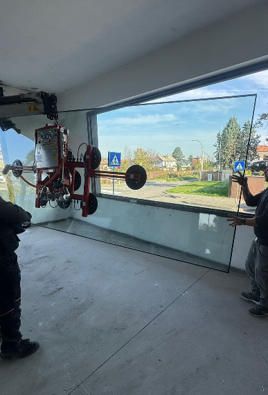 Gli operai utilizzano una macchina a vuoto per installare un grande pannello di vetro nel telaio di una finestra all'interno di un edificio non ancora ultimato.