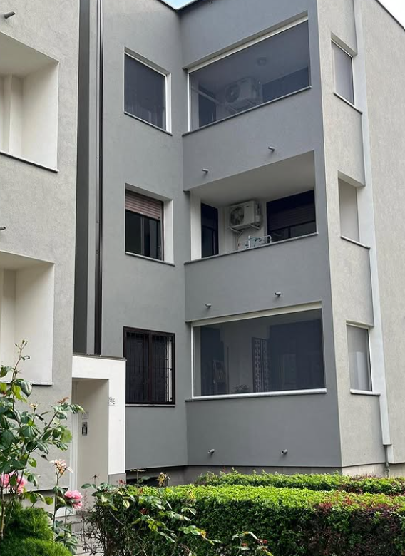 Un moderno edificio residenziale grigio a tre piani con balconi incassati e un piccolo giardino in primo piano.