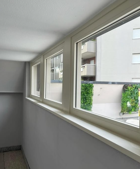 In una stanza bianca, una fila di tre finestre si affaccia sull'esterno di un edificio con un piccolo giardino verticale.