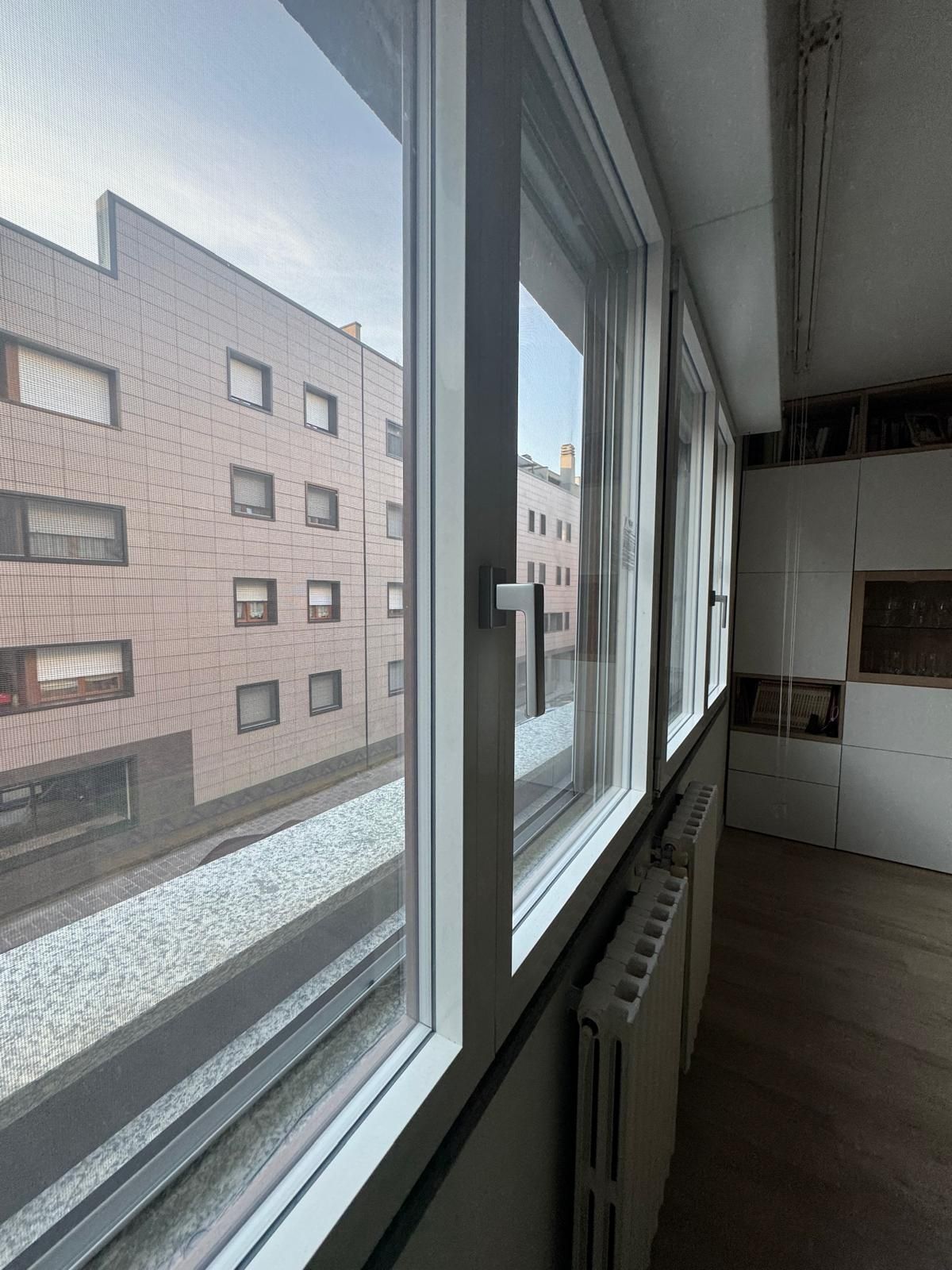 In una stanza bianca, una fila di tre finestre si affaccia sull'esterno di un edificio con un piccolo giardino verticale.