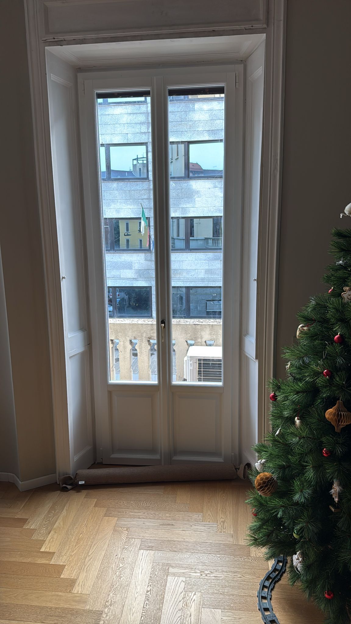 Una finestra con cornice bianca e due persiane verticali verdi si apre su una parete beige.