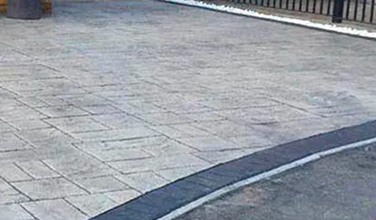 a concrete driveway with a black curb and a fence in the background .