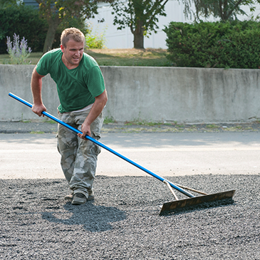 a man in a green shirt is raking gravel with a blue rake