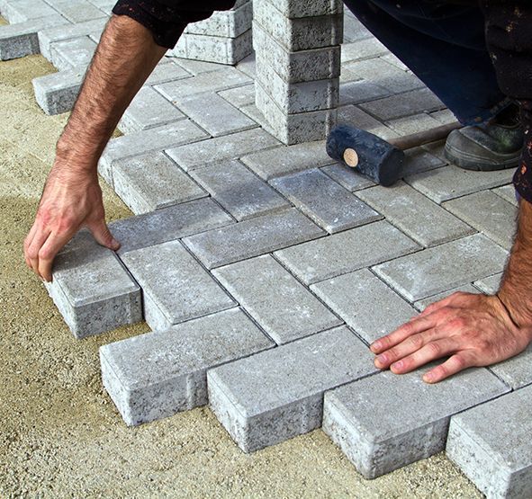 a man is laying bricks on the ground with a hammer .