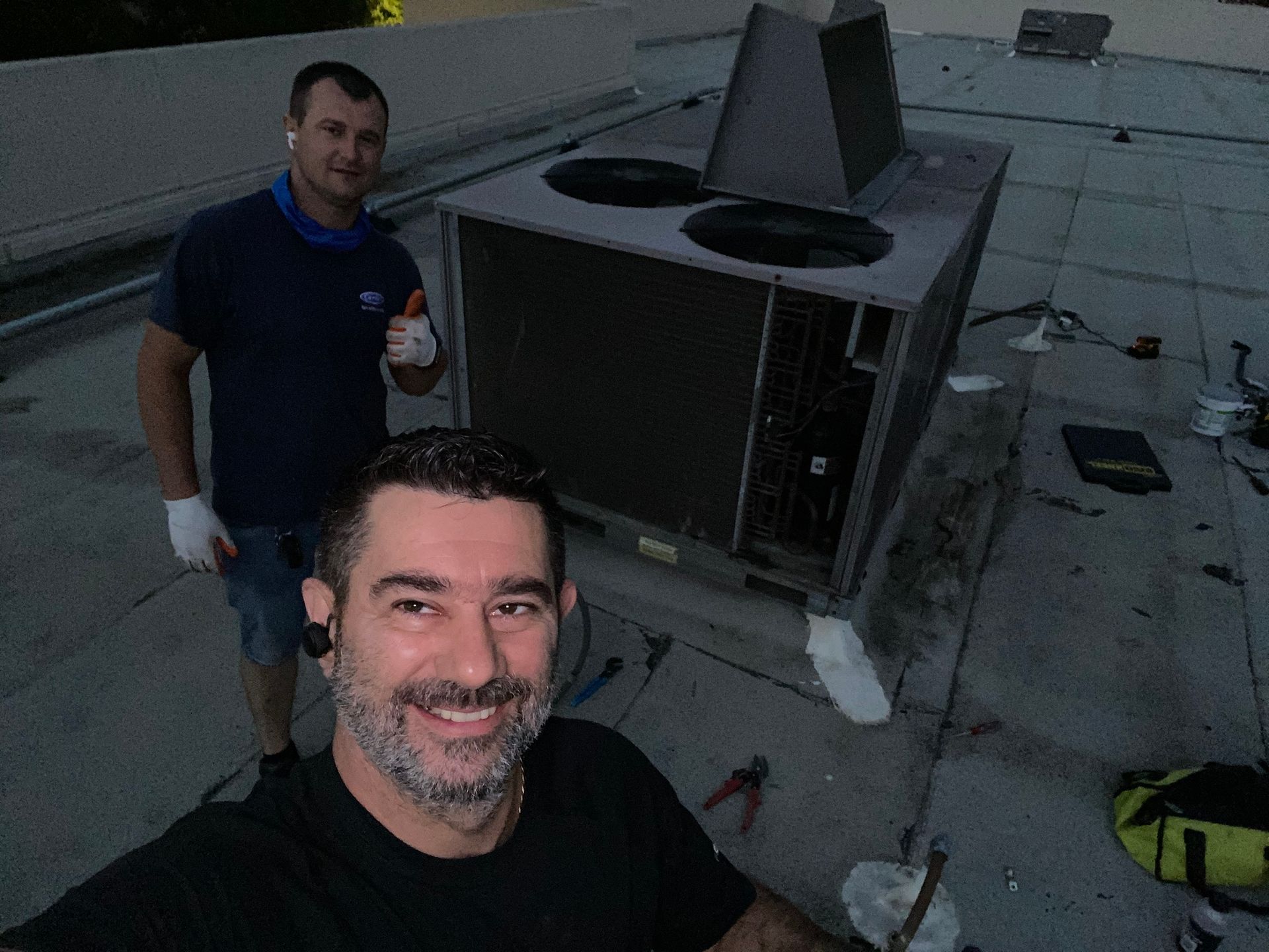 two men are standing next to a large air conditioner on a roof .