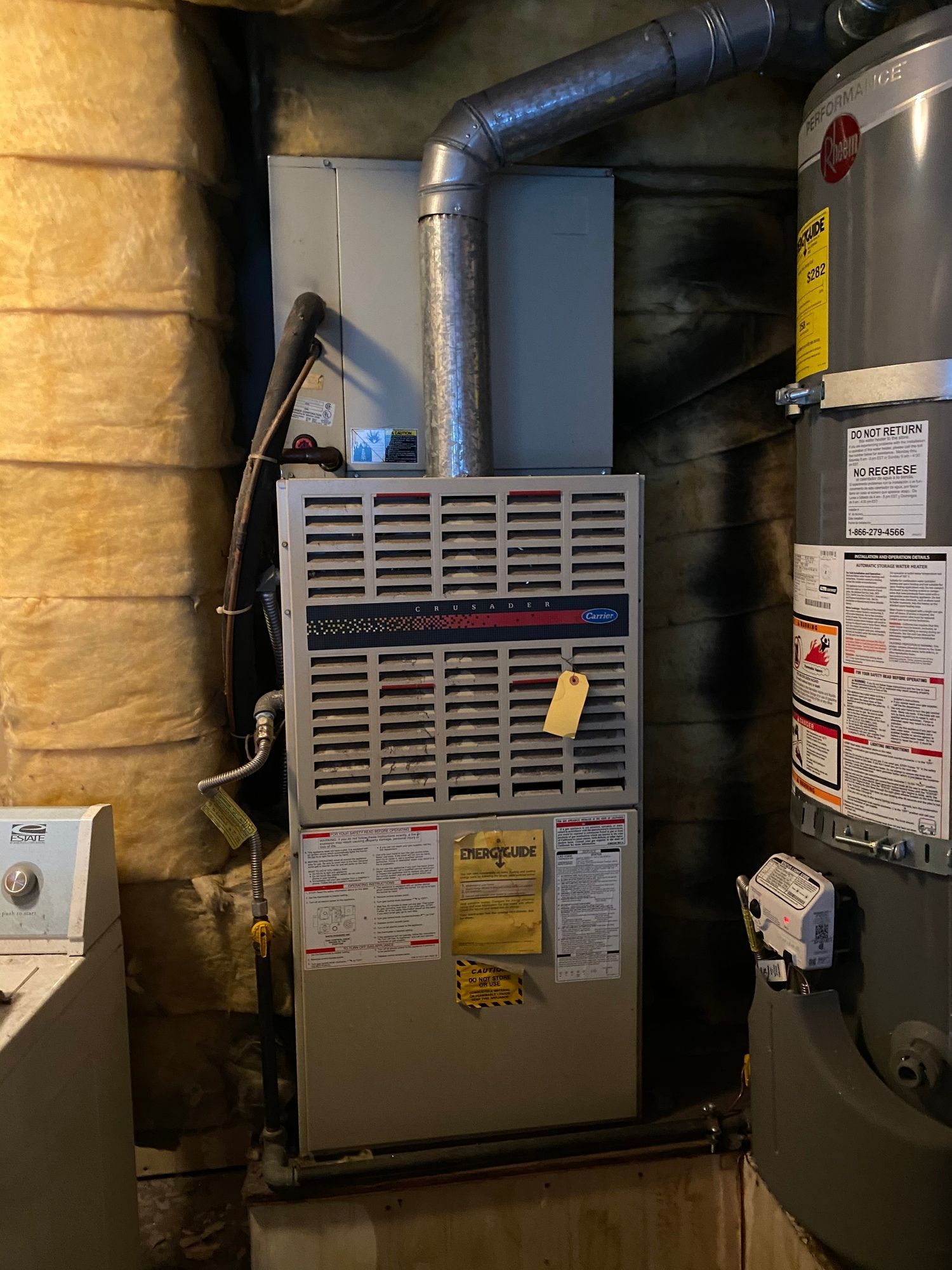 an air conditioner is sitting next to a water heater in a basement .