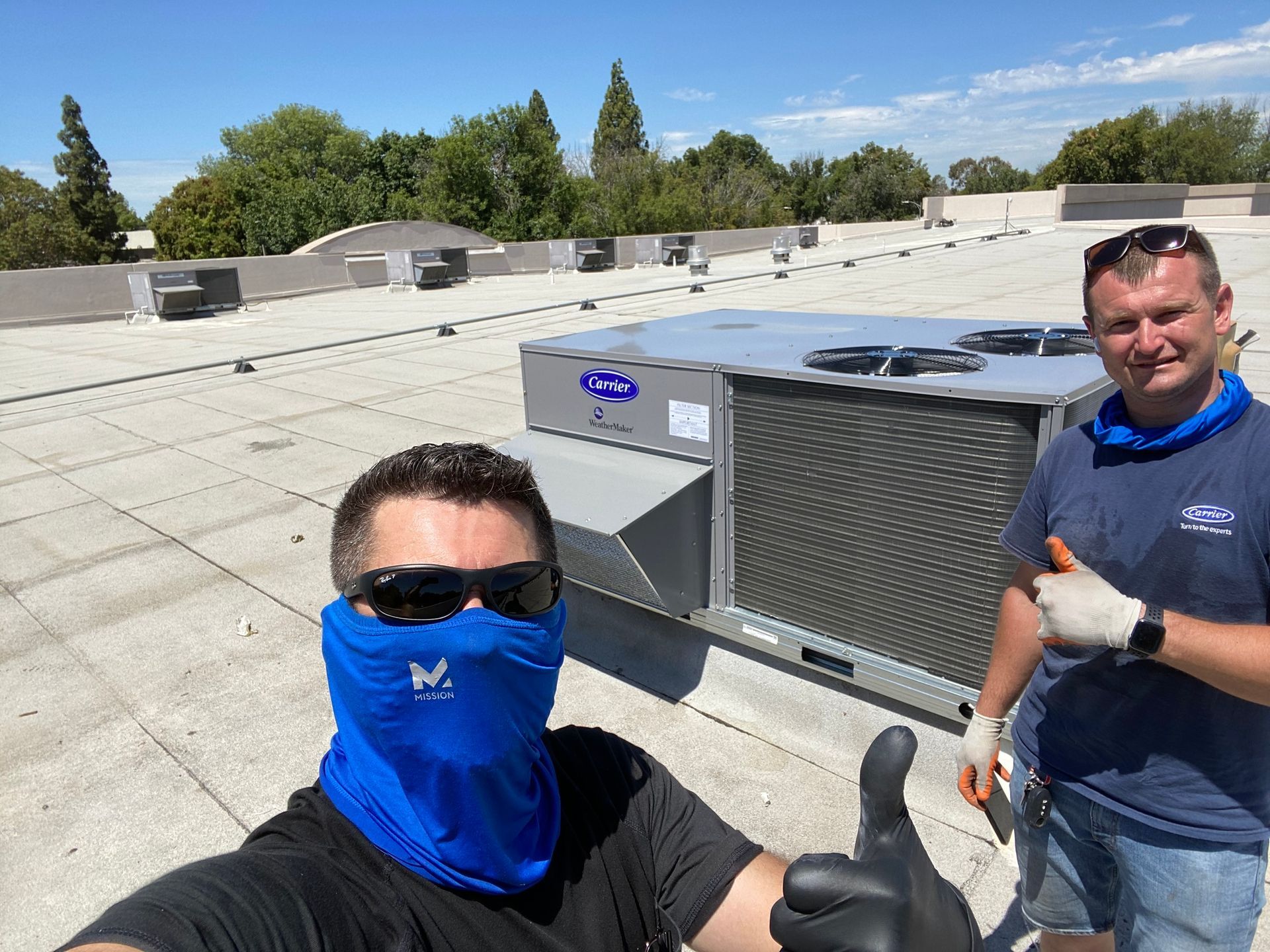 two men are standing on top of a roof giving a thumbs up .