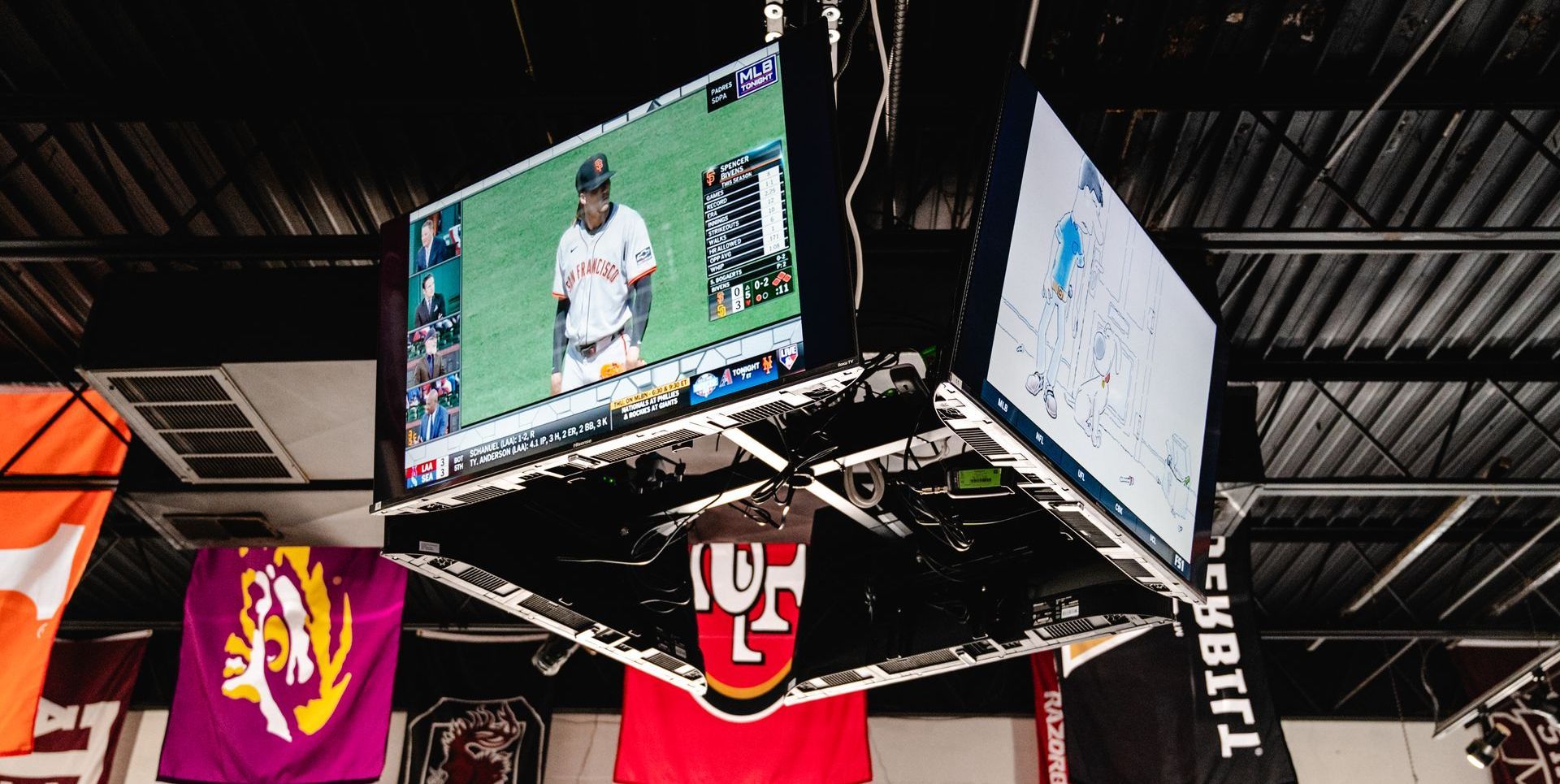 A tv is hanging from the ceiling in a room with flags hanging from the ceiling.