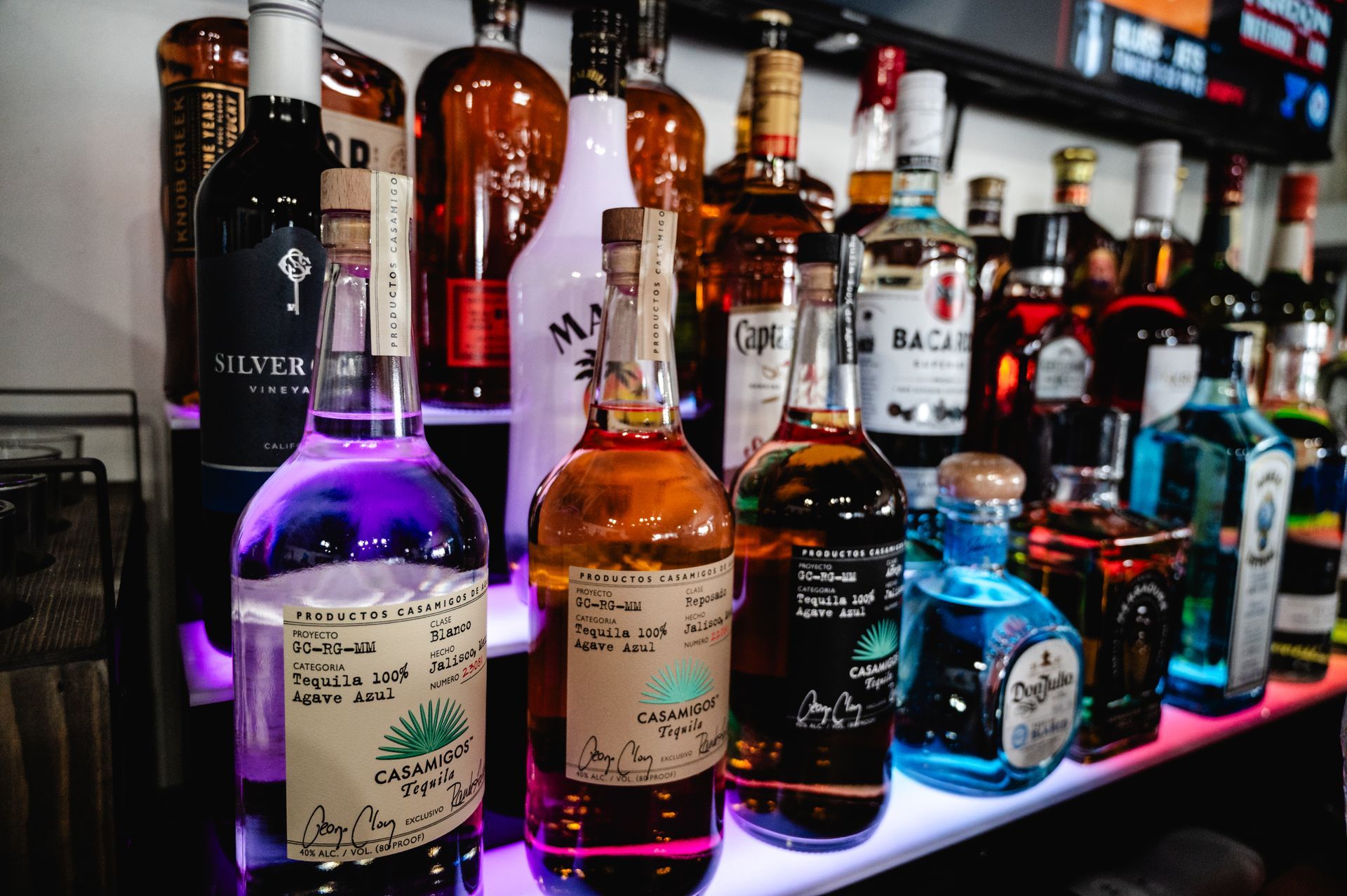 A row of bottles of liquor are lined up on a bar shelf.