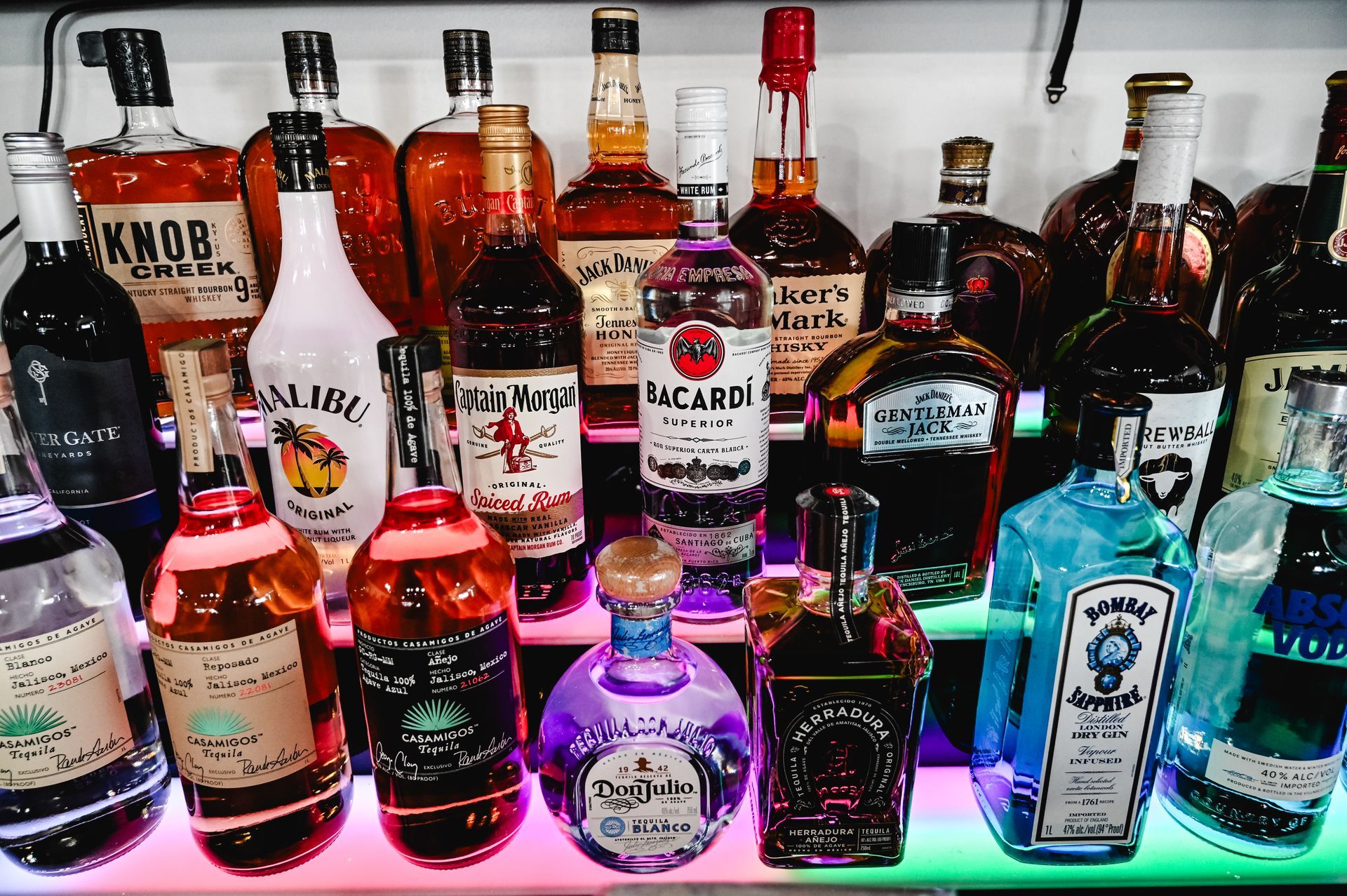 Many bottles of liquor are lined up on a shelf including jack daniels