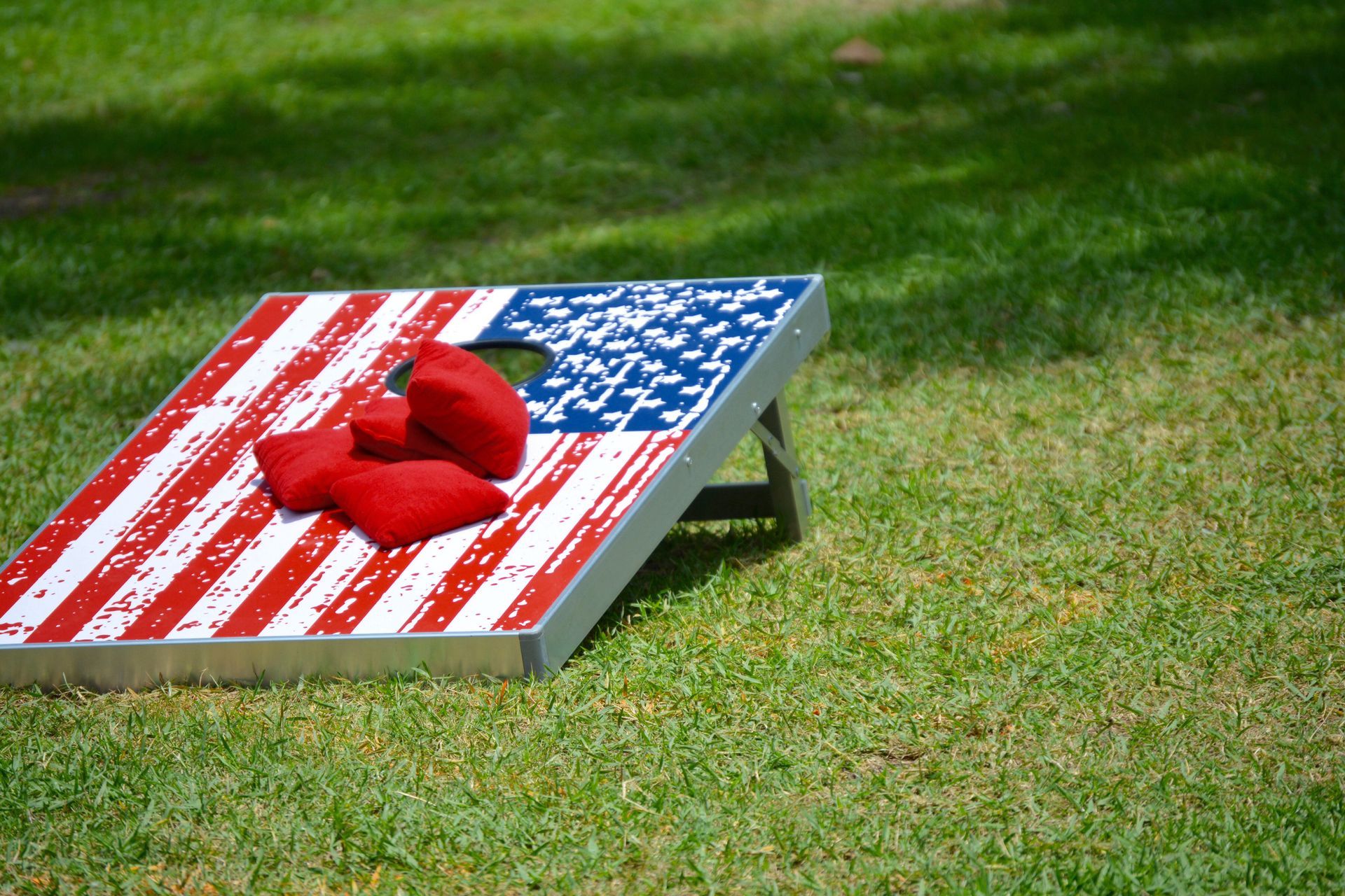 A cornhole board with an american flag on it is sitting in the grass.
