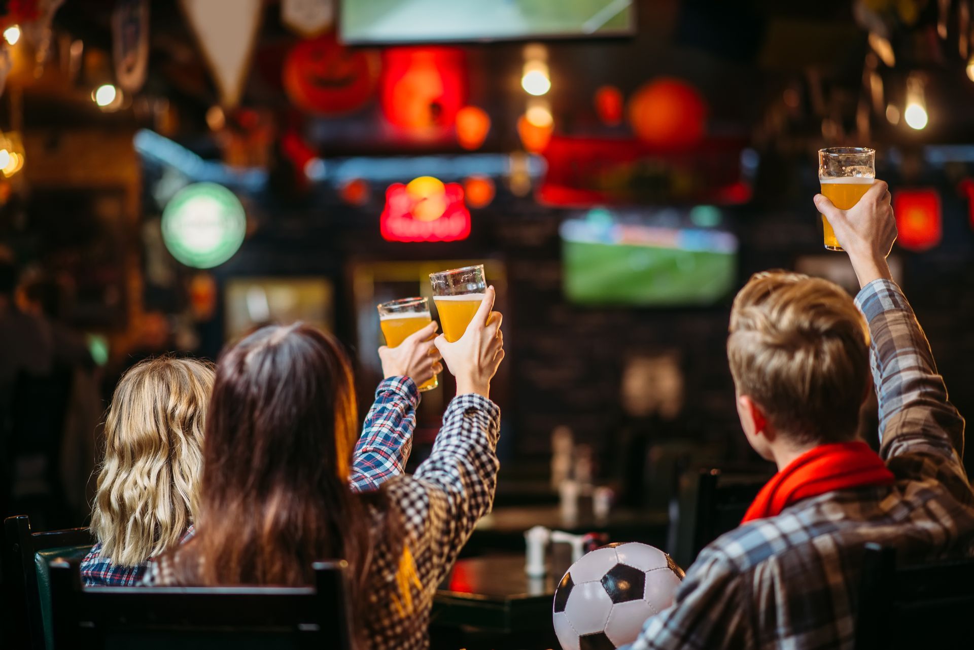 A group of people are sitting at a table in a bar holding up glasses of beer.