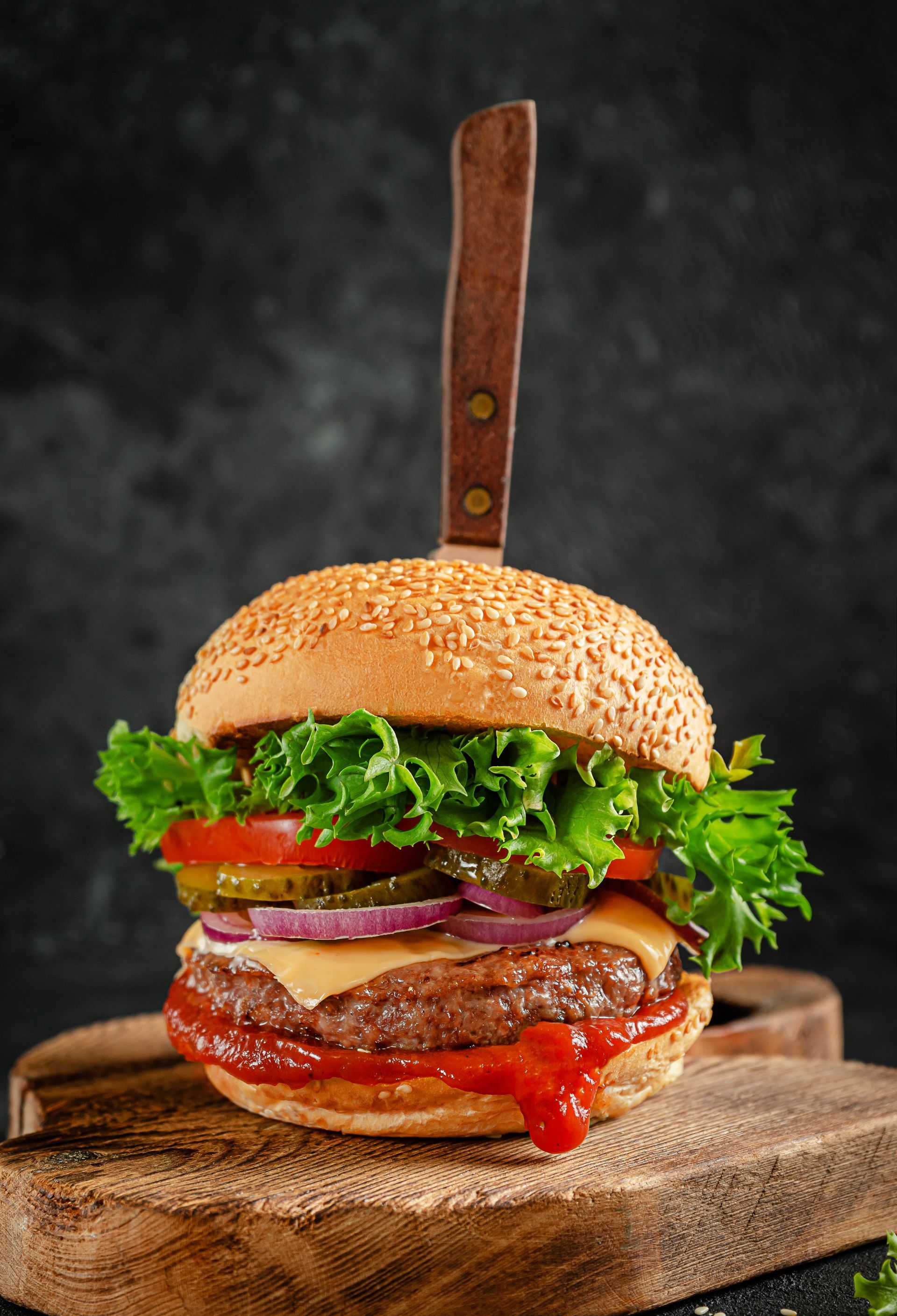 A hamburger with lettuce , tomatoes , onions and ketchup on a wooden cutting board.