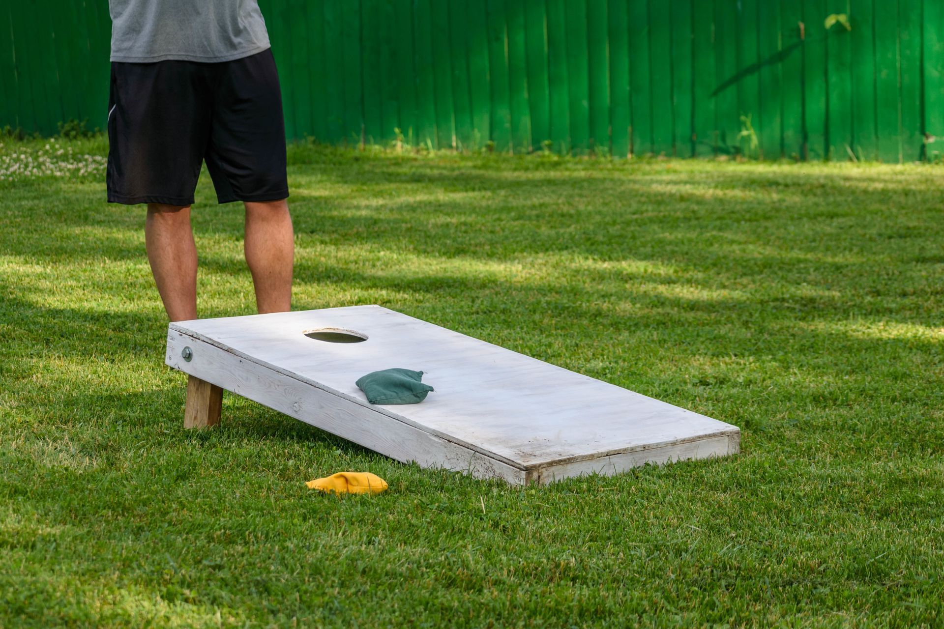 A man is playing a game of cornhole in the grass.