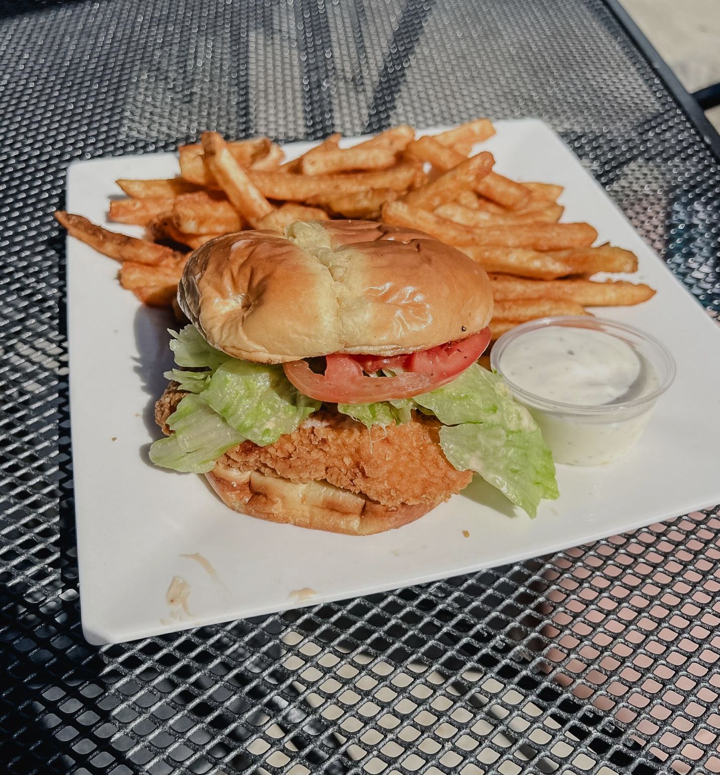 A hamburger is sitting on a cutting board next to a bottle of sauce.