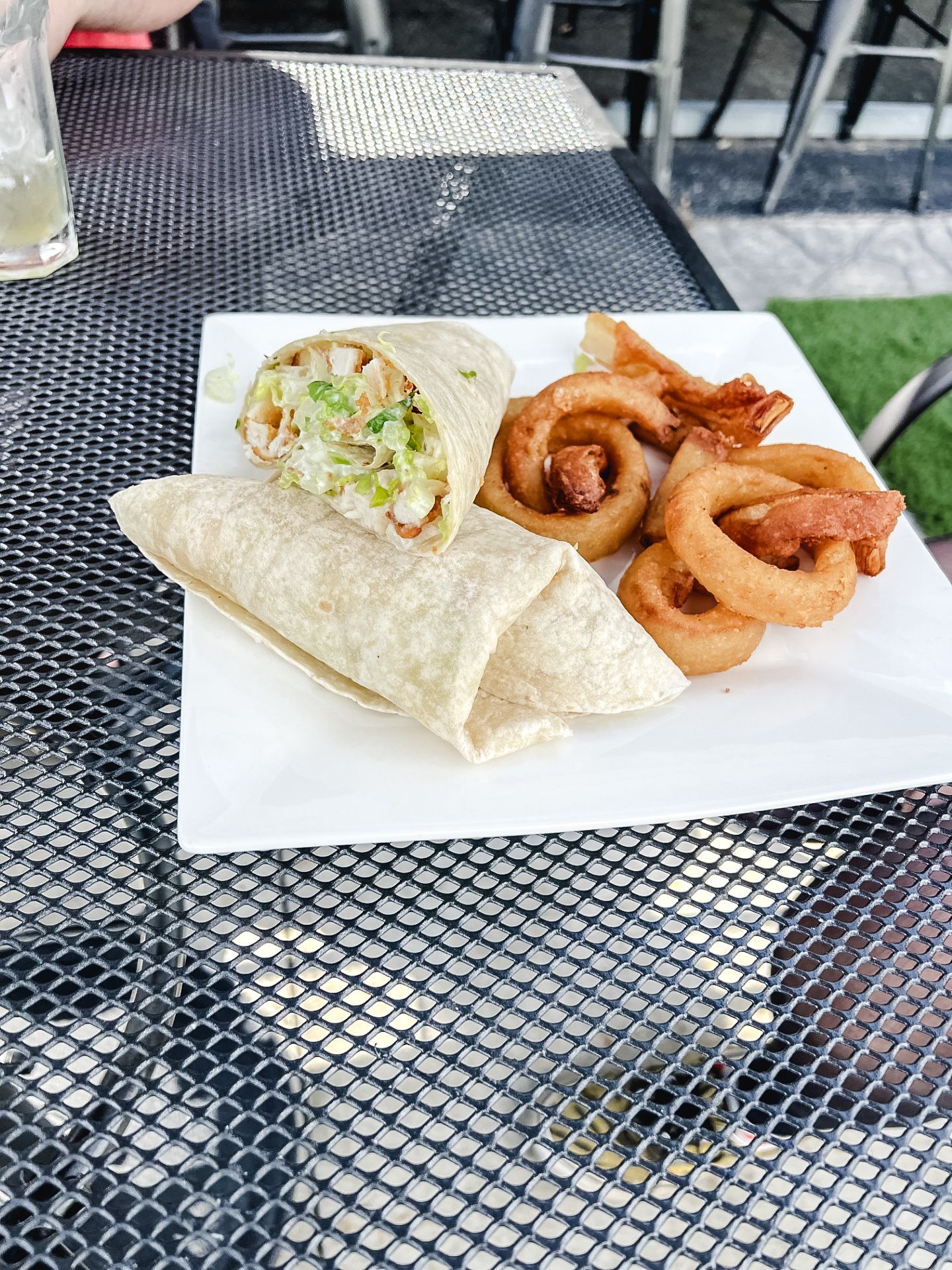 A tortilla wrap and onion rings are on a white plate on a table.