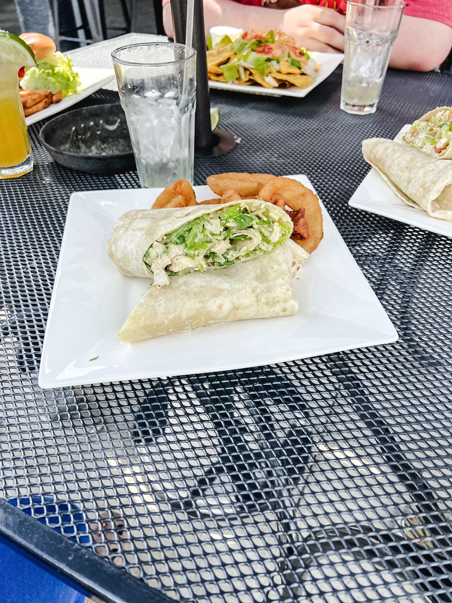 A white plate topped with a wrap and onion rings on a table.