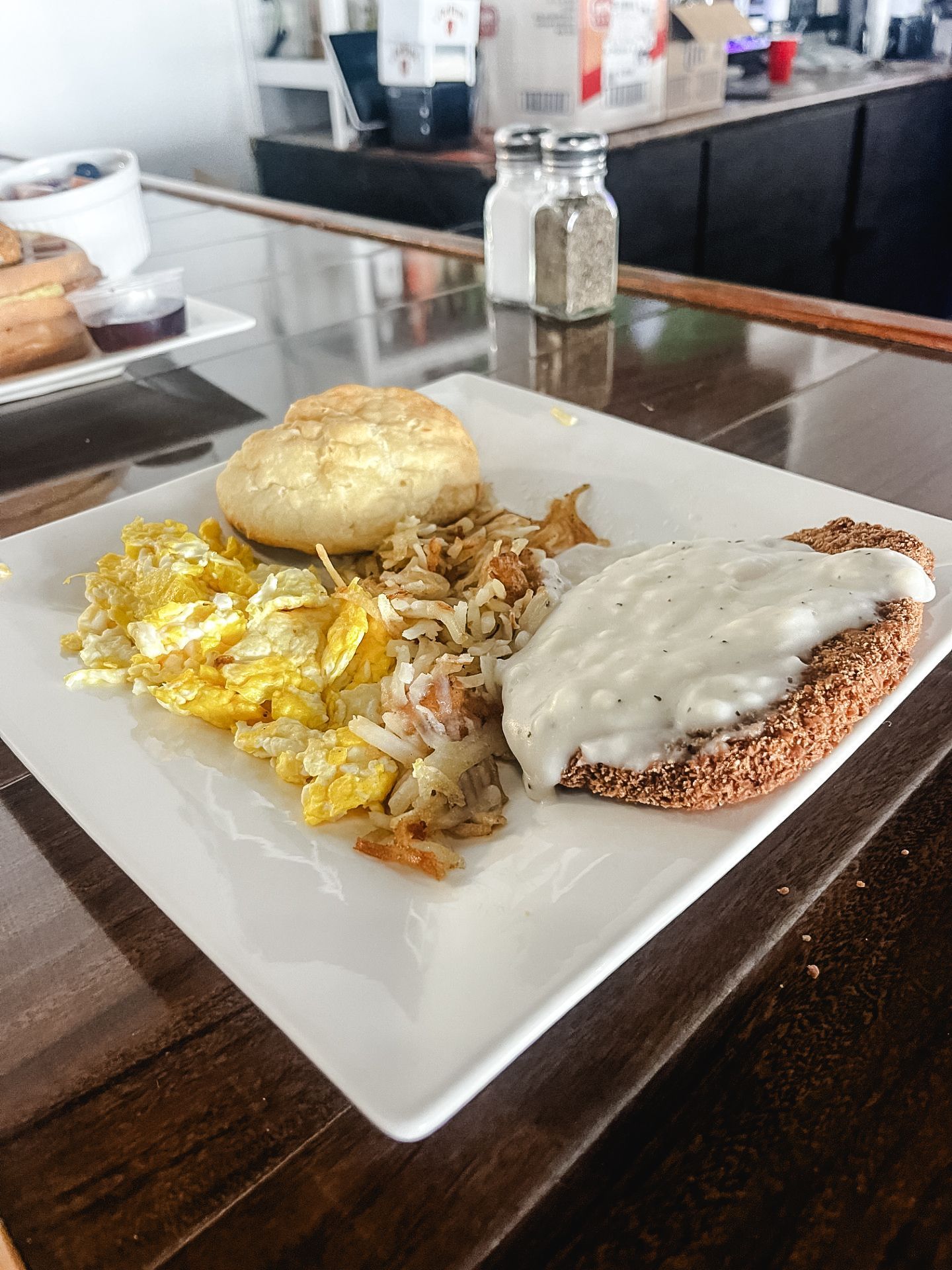 A white plate topped with scrambled eggs , gravy and a biscuit on a table.