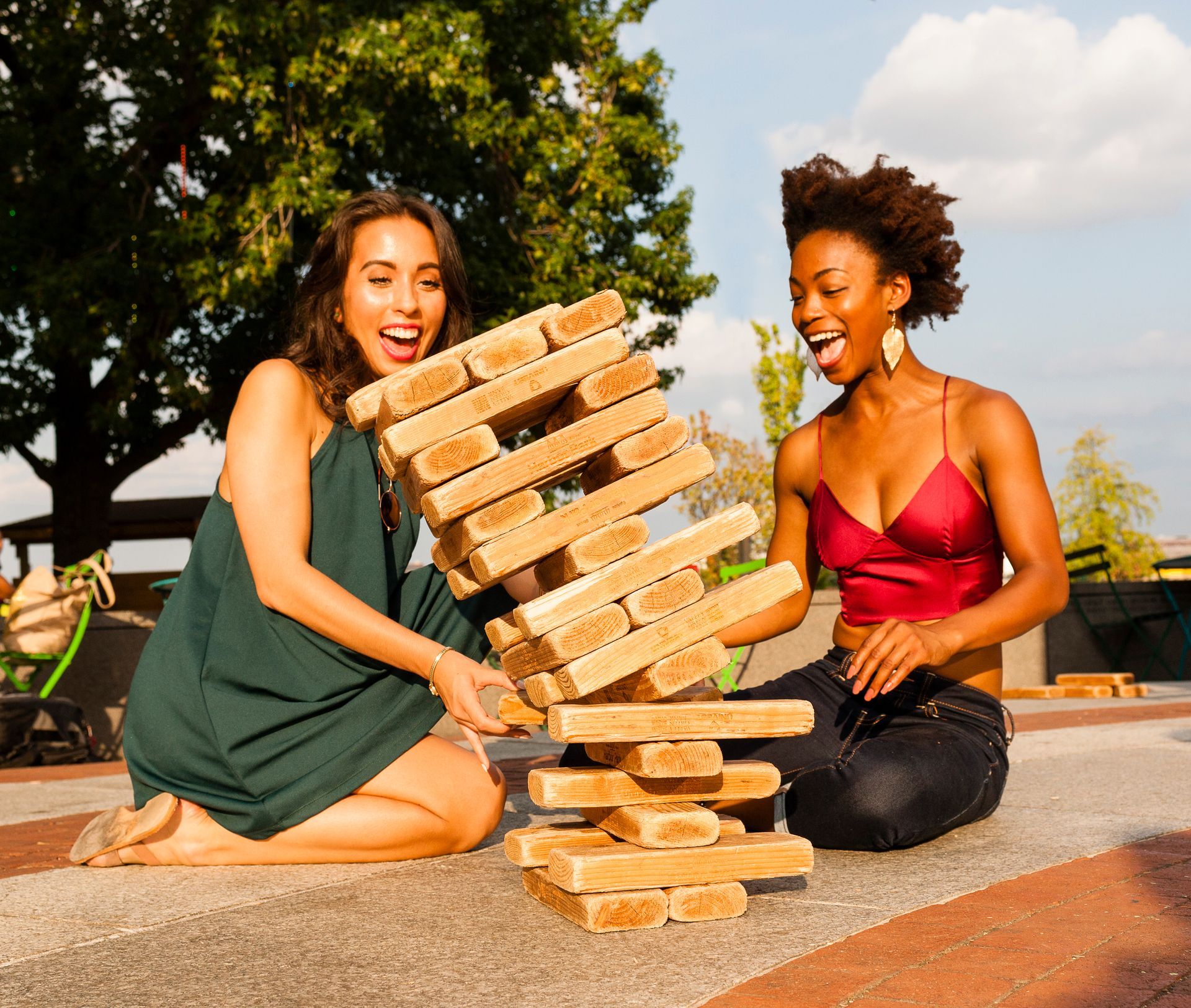 Two women are sitting on the ground playing a game of jenga.