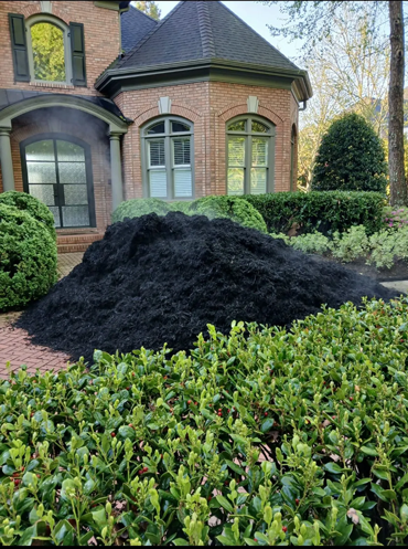 A large pile of black mulch is in front of a brick house.