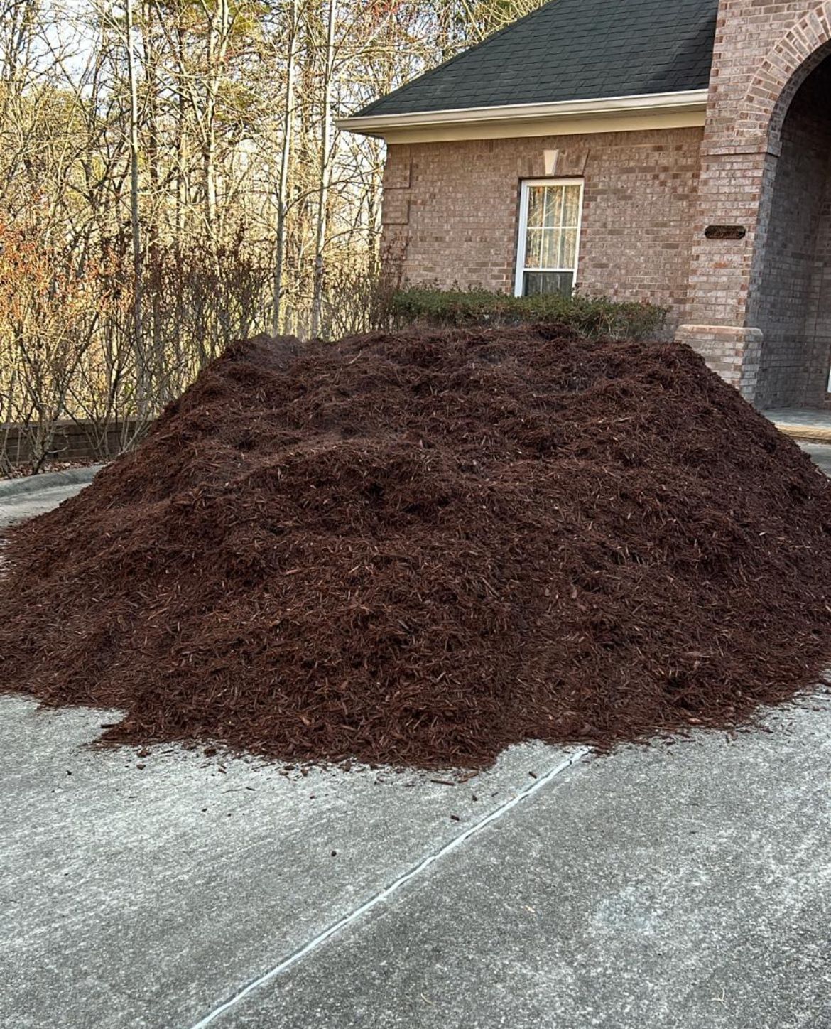 A large pile of mulch is sitting on the side of a road in front of a house. A large pile of mulch is sitting on the side of a road in front of a house.