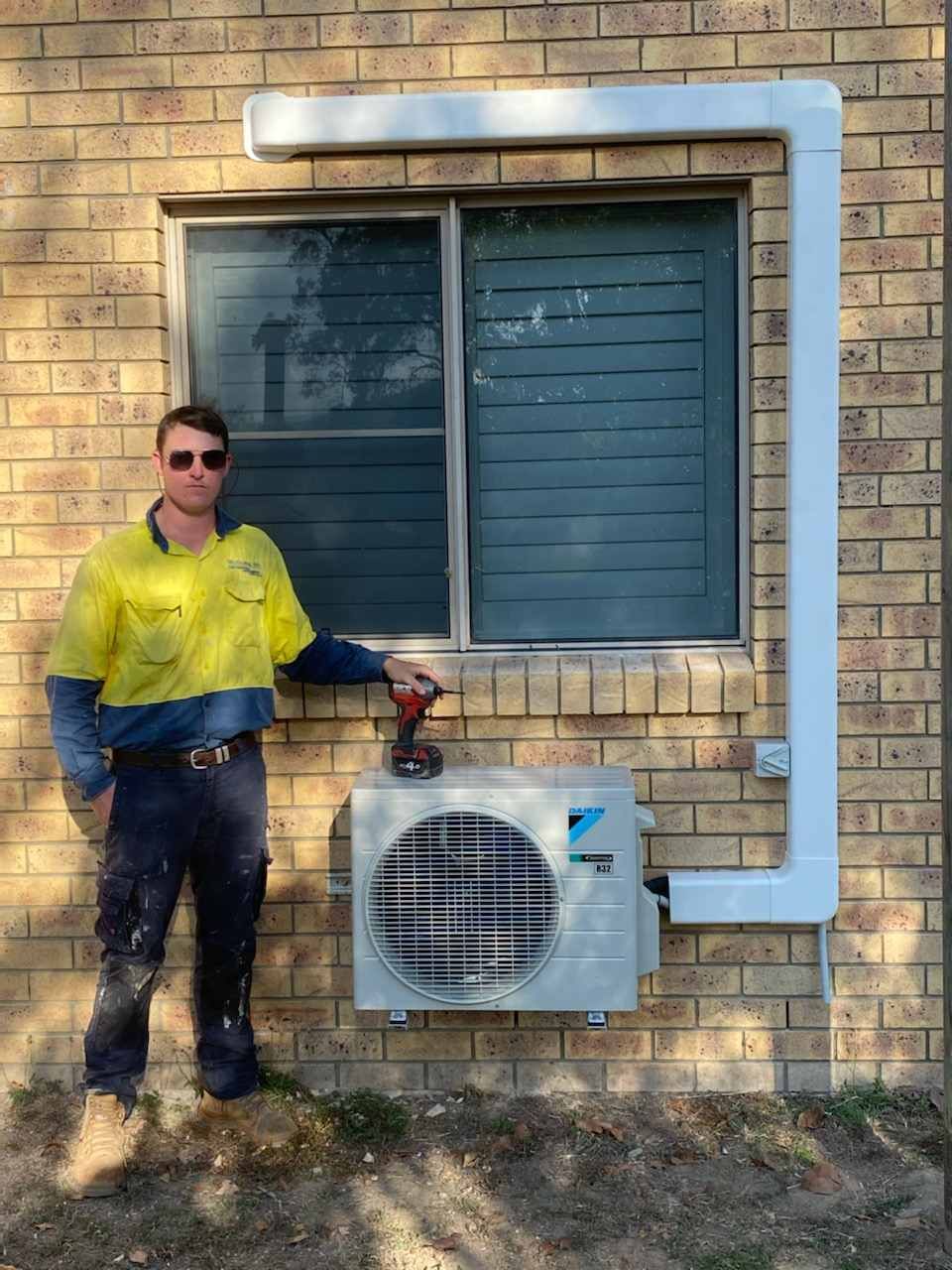 A Man Is Standing in Front of A Brick Wall Next to A Window — McGuire Air & Refrigeration In Paget, QLD