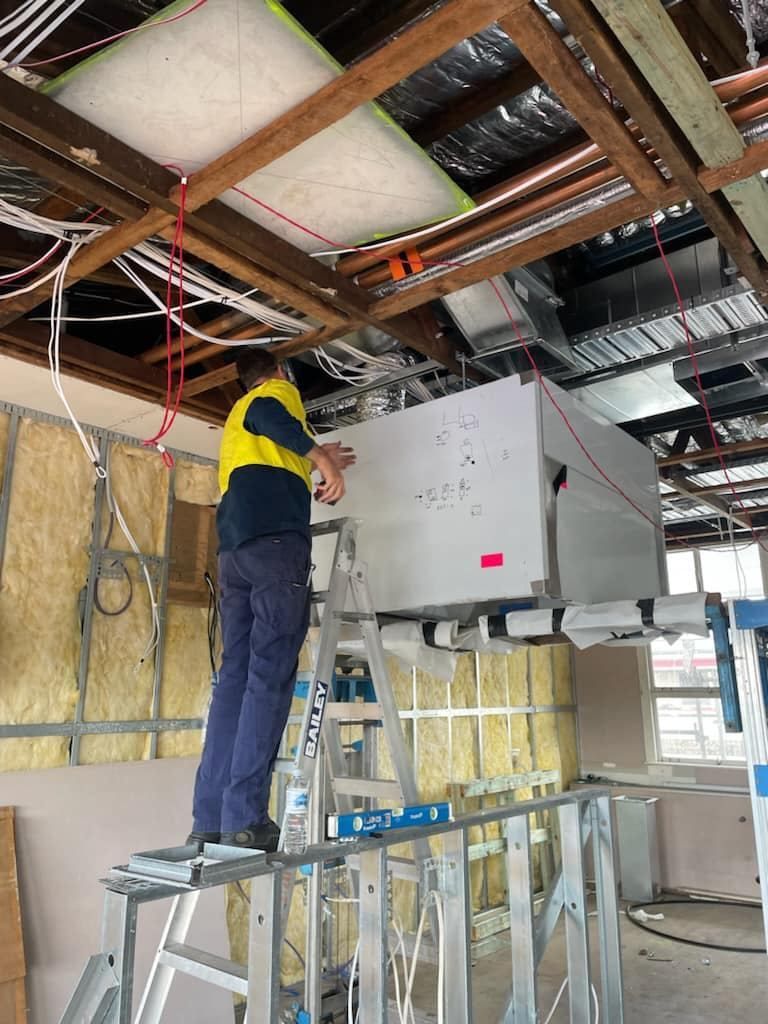 A Man Is Standing on A Ladder Working on A Ceiling — McGuire Air & Refrigeration In Paget, QLD